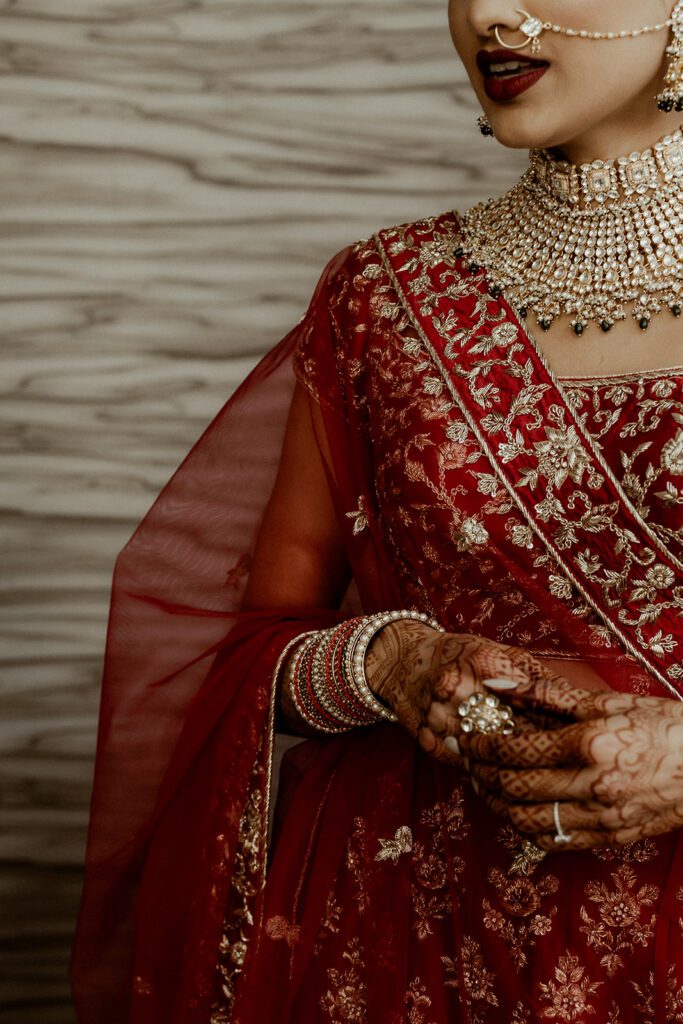Cinematic detail shot of Indian bride in red lehenga with mehndi and gold jewelry by Dallas South Asian wedding photographer William Bichara